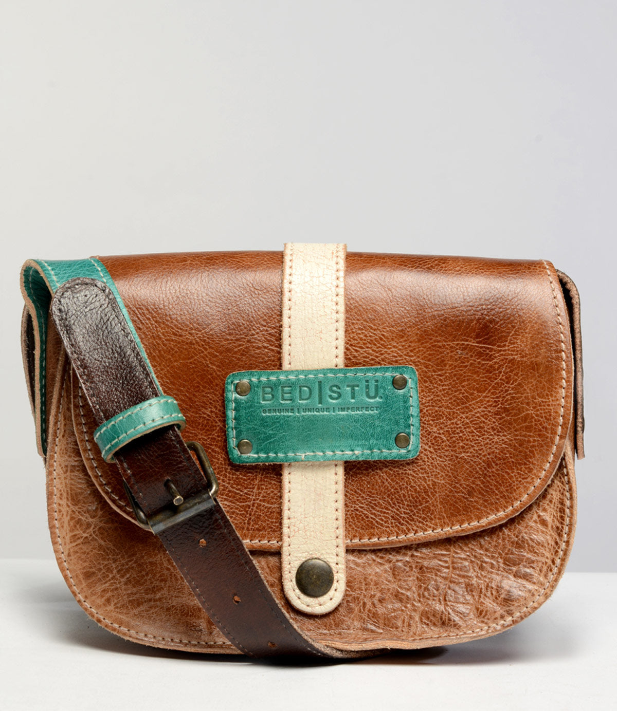 Introducing the Studio Shoreline Body crossbody bag by Bed|Stü: crafted in brown leather, featuring a beige vertical strap, a distinctive green accent patch with the "Bed|Stü" logo, and an adjustable shoulder strap edged in green. Set against a clean light backdrop, this customizable bag lets you express your personal style and create a look that’s all your own.