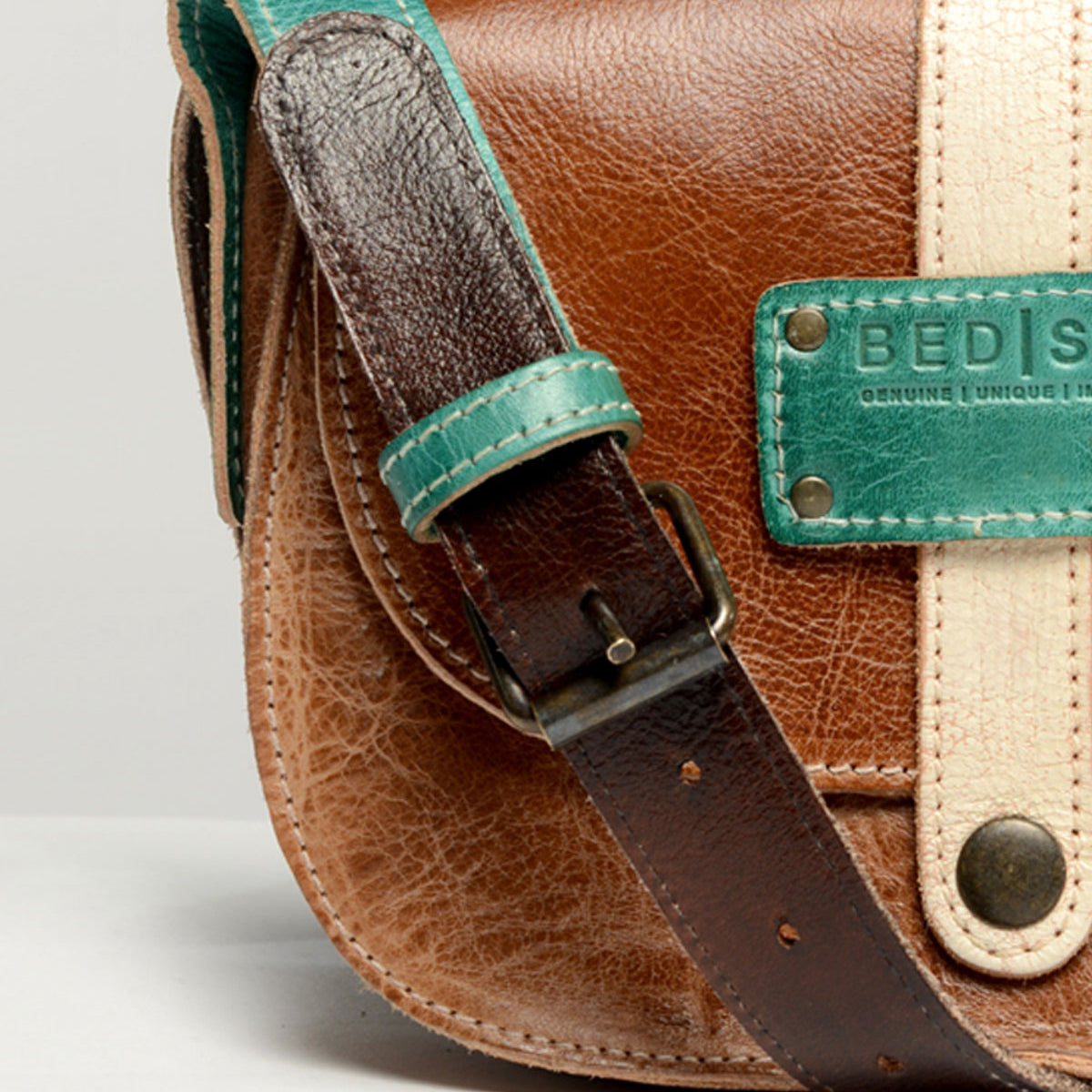 Close-up of the Studio Long Shoulder Strap by Bed|Stü, featuring brown leather with a teal strap and beige accent, complete with a metal plate and buckle—ideal for anyone seeking a customizable accessory to express their unique style.