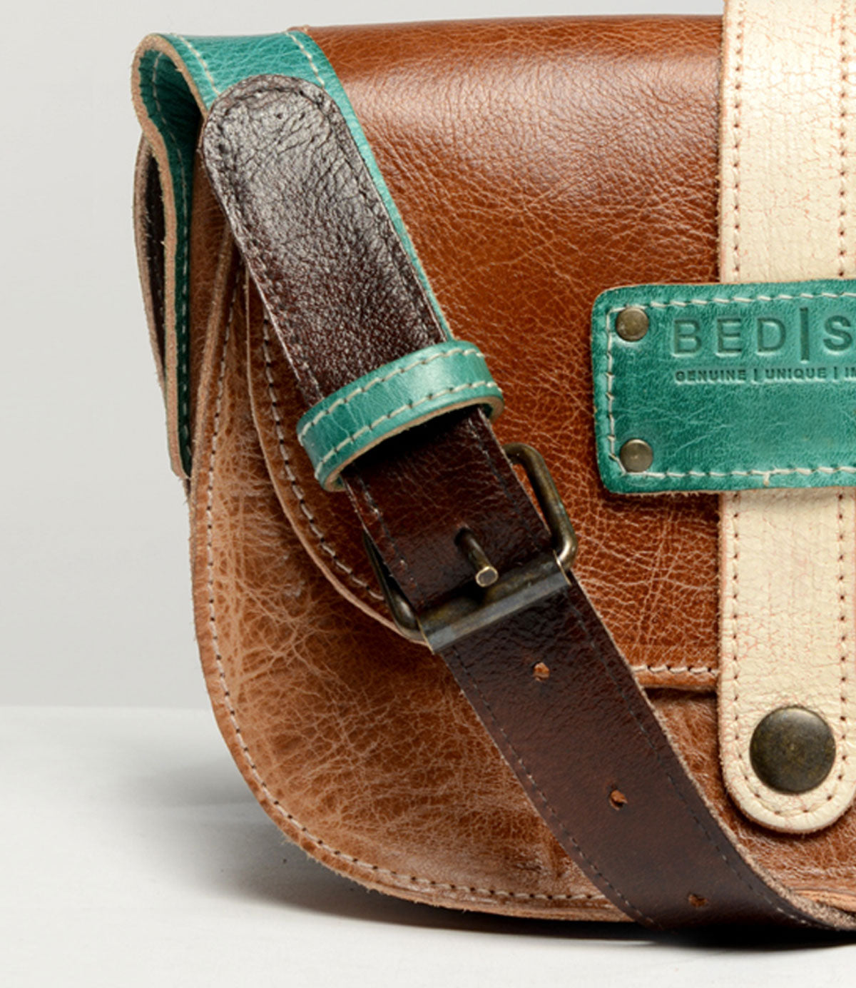 Close-up of the Studio Long Shoulder Strap by Bed|Stü, featuring brown leather with a teal strap and beige accent, complete with a metal plate and buckle—ideal for anyone seeking a customizable accessory to express their unique style.