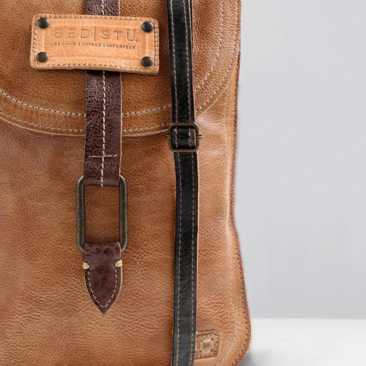 A close-up of a brown leather bag featuring the Bed|Stü Studio Thin Shoulder Strap in black—an adjustable option with a buckle detail on the flap, ideal for those who want a bag that showcases their unique style.