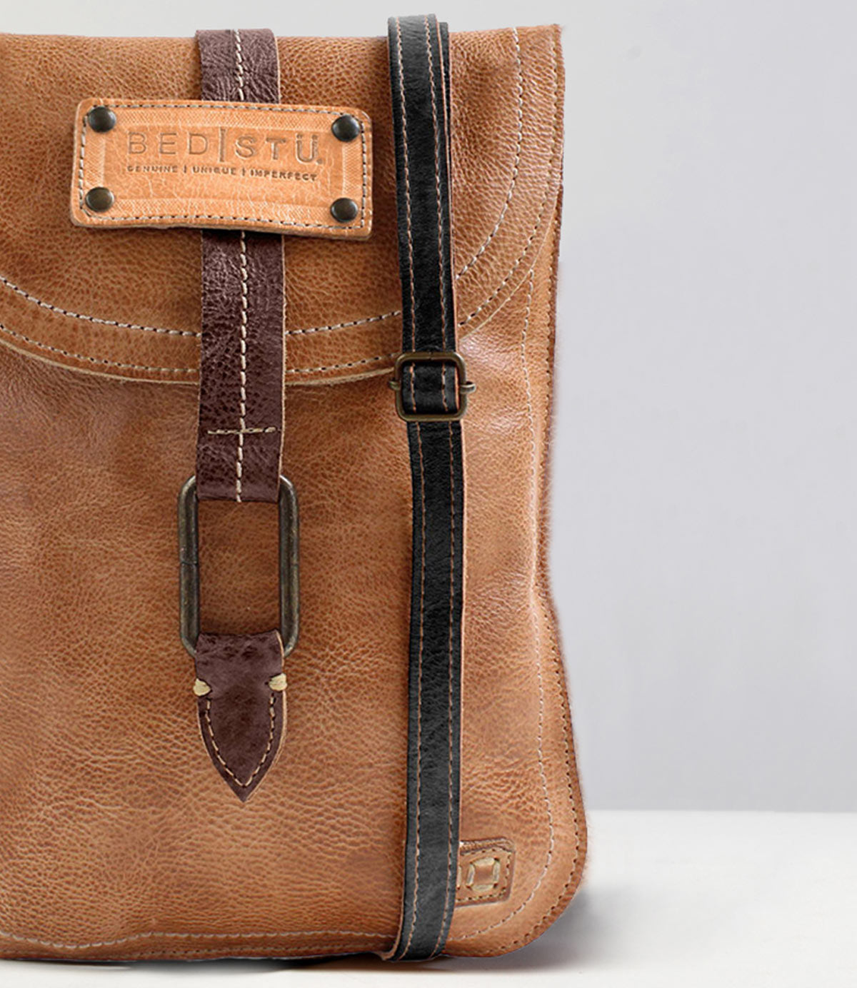 A close-up of a brown leather bag featuring the Bed|Stü Studio Thin Shoulder Strap in black—an adjustable option with a buckle detail on the flap, ideal for those who want a bag that showcases their unique style.