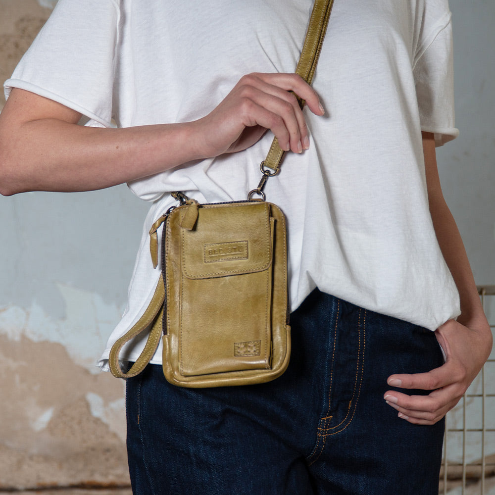 Person wearing a small olive leather crossbody bag over a white T-shirt and dark jeans.