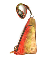 Introducing the Adept by Bed|Stü: a triangular crossbody crafted from vegetable-tanned leather in a striking red, green, and tan gradient. This compact sling features a front zipper and comes with a matching adjustable strap laid above the bag, making it perfect for carrying your everyday essentials.