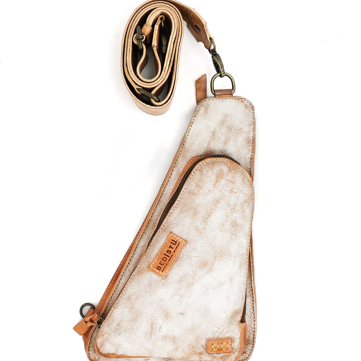 The Bed|Stü Adept is a compact sling crafted from tan and white vegetable-tanned leather, featuring an attached zippered pocket and shown with its adjustable strap coiled above the bag on a white background.