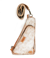 The Bed|Stü Adept is a compact sling crafted from tan and white vegetable-tanned leather, featuring an attached zippered pocket and shown with its adjustable strap coiled above the bag on a white background.