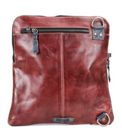 Introducing the Aiken by Bed|Stü—a square-shaped, brown full-grain leather bag featuring a front zipper pocket, visible stitching, and distinctive metal rings positioned on the top right and bottom left corners. This stylish accessory comes with an adjustable strap for comfortable carrying.