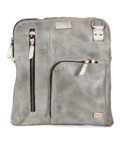Introducing the Aiken by Bed|Stü—a square crossbody crafted from light gray full-grain leather, featuring two zippered pockets on the front, a small patch label, and a silver D-ring near the top right corner. The adjustable strap ensures comfortable and versatile wear.