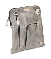 The Bed|Stü Aiken is a grey full-grain leather crossbody bag featuring multiple zippered pockets, beige accents, and an adjustable strap, shown standing upright against a white background.
