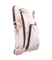 The Bed|Stü Aiken is a light brown, distressed full-grain leather crossbody bag featuring two zippered compartments and an adjustable strap, shown standing upright on a white background.