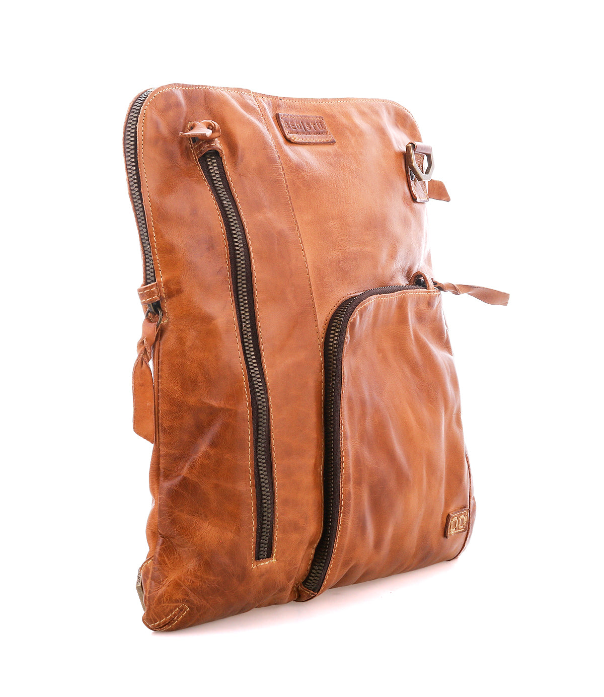 Bed|Stü’s Aiken is a tan full-grain leather shoulder bag, shown against a white background. It features two visible zippered pockets—one vertical and one diagonal—and an adjustable strap for comfortable carrying.