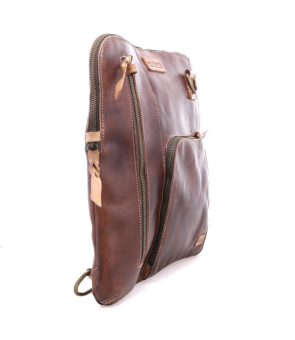 The Bed|Stü Aiken is a brown full-grain leather zippered pouch shown standing upright at an angle, featuring two zippered compartments, anti-theft security features, and a brand tag on the front.