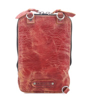The Alelike by Bed|Stü is a small, rectangular crossbody bag crafted from red-brown leather, featuring a zipper closure, metal rings, and a textured, worn finish—perfect for carrying your travel essentials in a stylish and compact purse.