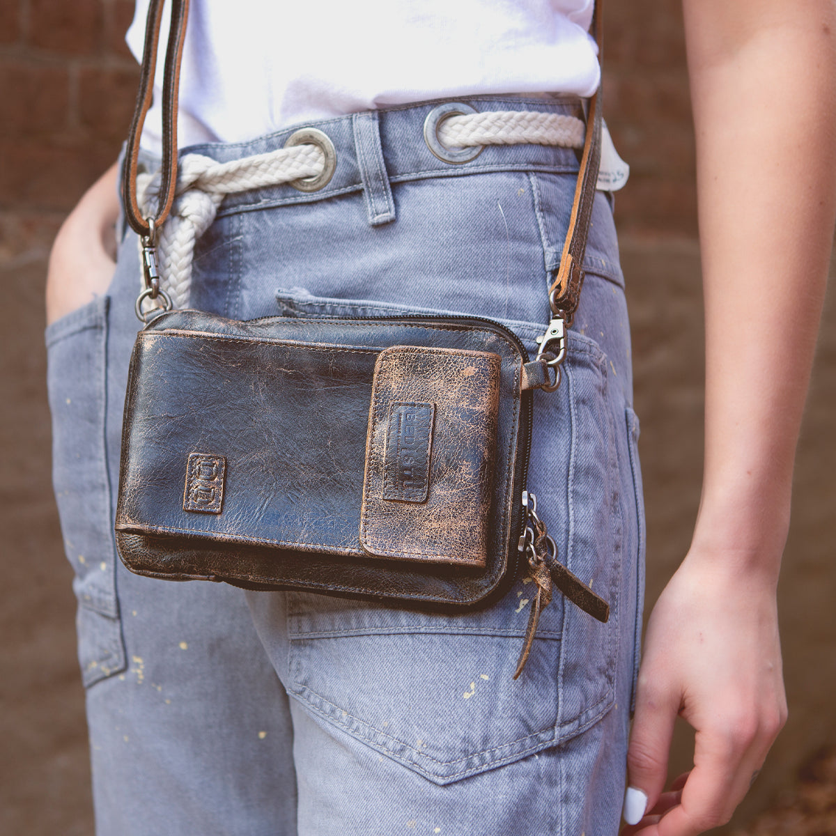 Wearing blue jeans and a white shirt with a white rope belt, this person carries the Bed|Stü Alelike leather crossbody bag—a compact purse perfect for travel essentials—with keys attached.