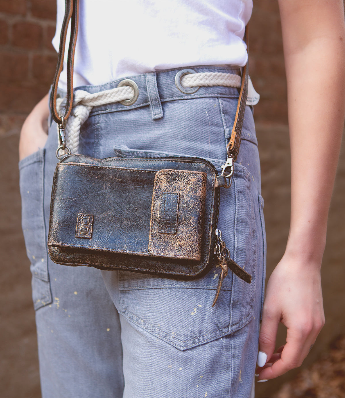 Wearing blue jeans and a white shirt with a white rope belt, this person carries the Bed|Stü Alelike leather crossbody bag—a compact purse perfect for travel essentials—with keys attached.