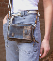 Wearing blue jeans and a white shirt with a white rope belt, this person carries the Bed|Stü Alelike leather crossbody bag—a compact purse perfect for travel essentials—with keys attached.