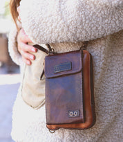A person wearing a textured cream jacket holds the Bed|Stü Alelike leather crossbody bag, featuring visible stitching and hardware details—the perfect companion for carrying travel essentials in style.