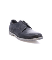 The Bed|Stü Anchiano is a black leather lace-up oxford shoe featuring distressed leather and a slightly worn grey, flexible sole, photographed against a white background.