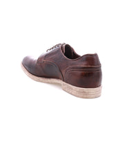 The Bed|Stü Anchiano is a brown distressed leather oxford shoe with laces, shown from the rear to highlight its worn sole and scuffed heel against a white background.