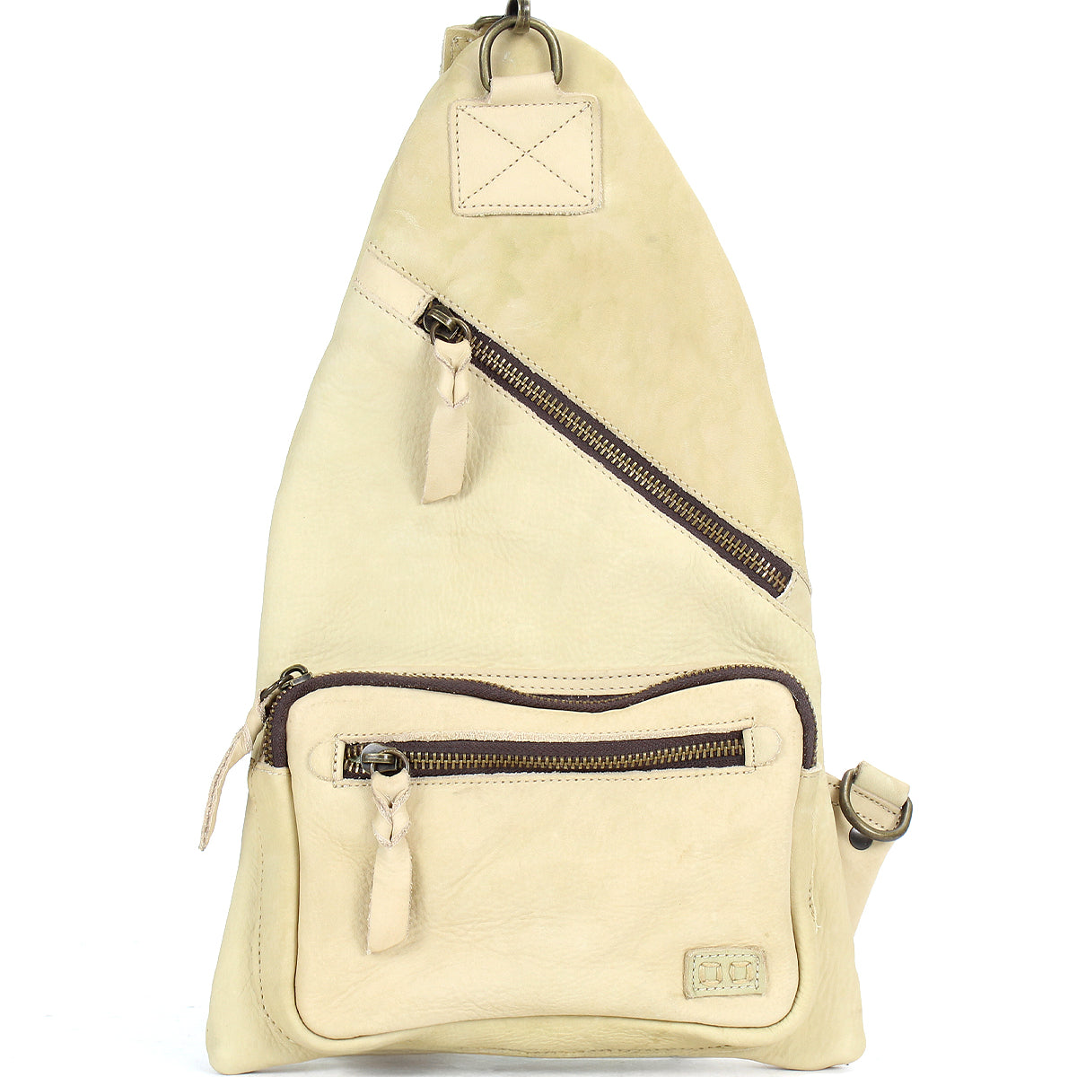 The Bed|Stü Andie is a beige leather sling bag featuring two zippered pockets and an adjustable strap, shown standing upright against a white background.