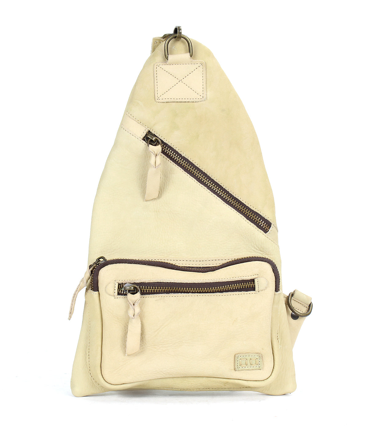 The Bed|Stü Andie is a beige leather sling bag featuring two zippered pockets and an adjustable strap, shown standing upright against a white background.