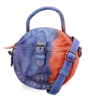 The Arenfield by Bed|Stü is a round leather crossbody bag featuring a top handle, front buckle detail, and an adjustable shoulder strap, designed with a striking blue and red gradient color pattern and secured with a zip-top closure.