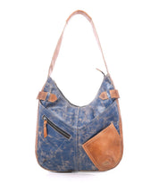Introducing the Argus by Bed|Stü—a handcrafted blue and brown patchwork leather shoulder bag featuring a large handle, convenient front zipper pocket, and an angled brown accent pocket. This stylish and functional bag is perfect for everyday use.