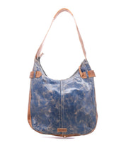 The Bed|Stü Argus is a blue and brown handcrafted leather shoulder bag featuring a single strap, visible stitching, and a slightly distressed finish. Photographed against a white background, this patchwork leather bag brings unique character to any outfit.