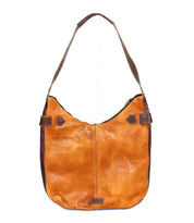 The Bed|Stü Argus is a brown patchwork leather bag with a wide strap and darker brown side accents, featuring oversized front pockets, shown against a white background.