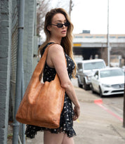 A woman in a black polka dot dress and sunglasses stands on a sidewalk, carrying the limited edition Bed|Stü Ariel EM tote over her shoulder.