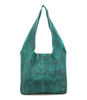The Ariel Max by Bed|Stü is a teal hand-finished leather shoulder bag with wide straps, a square front pocket, decorative stitching, and a small metal logo in the lower right corner. This oversized tote offers a spacious interior and is shown against a plain white background.