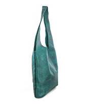 The Bed|Stü Ariel Max, a teal leather shoulder bag with a single wide strap and hand-finished details for a luxurious touch, is shown standing upright on a white background. Its spacious interior ensures it’s as practical as it is stylish.