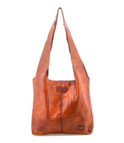 The Ariel Mid by Bed|Stü is an artisanal brown shoulder bag crafted from vegetable-tanned leather, featuring a wide strap, front stitching details, and a small rectangular patch near the bottom corner, displayed on a white background.