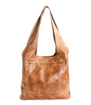 The Ariel EM by Bed|Stü is a light brown minimalist tote bag featuring a wide shoulder strap and two front pockets, displayed standing upright against a white background.