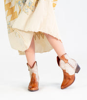 A person wearing a cream patchwork dress and the Bed|Stü Baila II light brown Western-inspired boots with a pointed toe, standing with legs crossed against a white background.