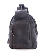 The Beau by Bed|Stü is a black leather sling backpack featuring a zipper front pocket and a top handle, photographed against a white background. This compact bag combines the versatility and convenience of a modern leather sling, making it perfect for everyday use.