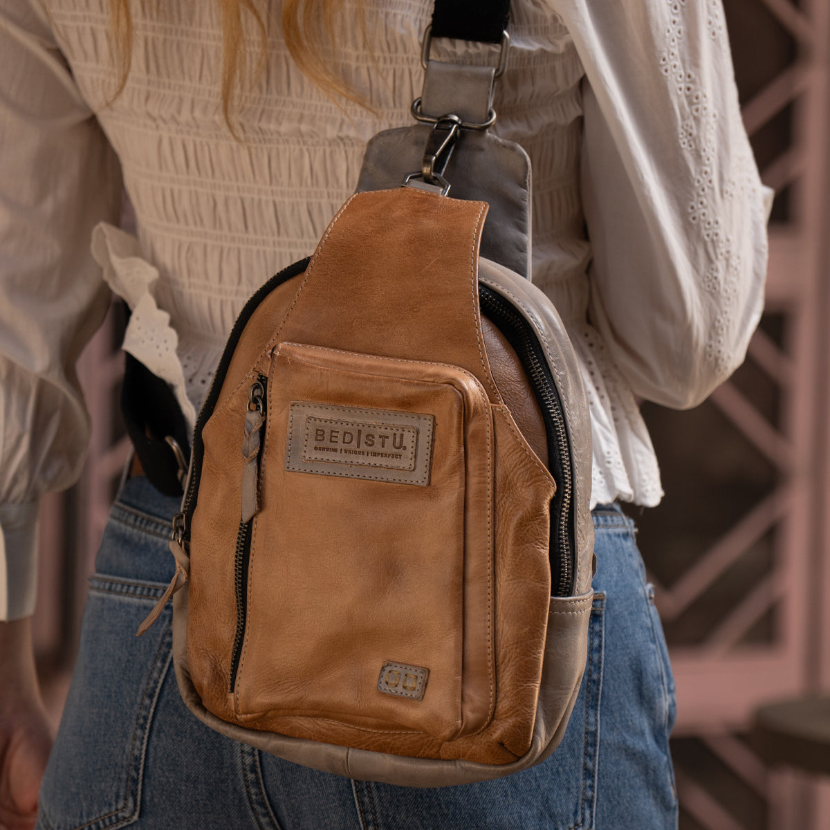 Person wearing the Bed|Stü Beau tan leather sling backpack over a white textured blouse and blue jeans, shown from the back.
