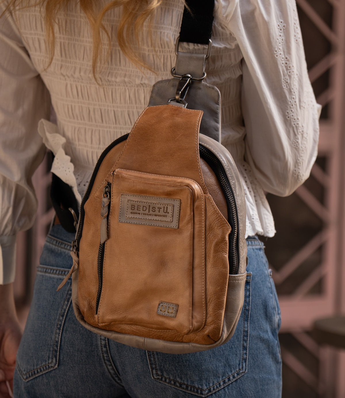 Person wearing the Bed|Stü Beau tan leather sling backpack over a white textured blouse and blue jeans, shown from the back.