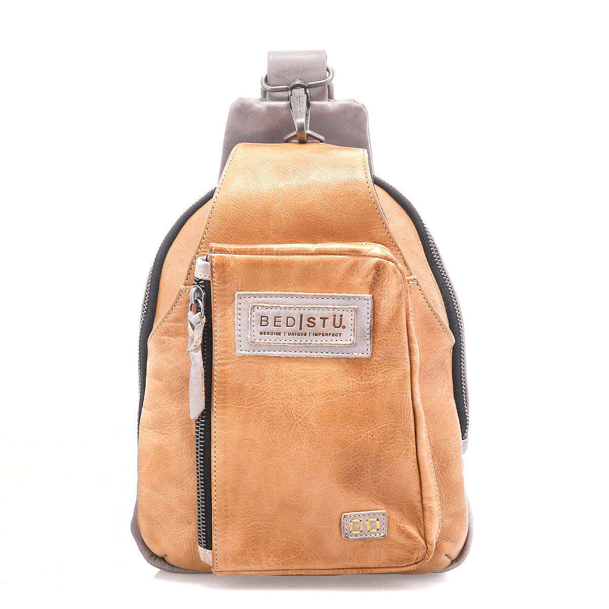 The Beau backpack by Bed|Stü is a compact tan leather sling with a front zipper pocket, signature "BED|STU" patch, and a single adjustable strap, shown against a white background.