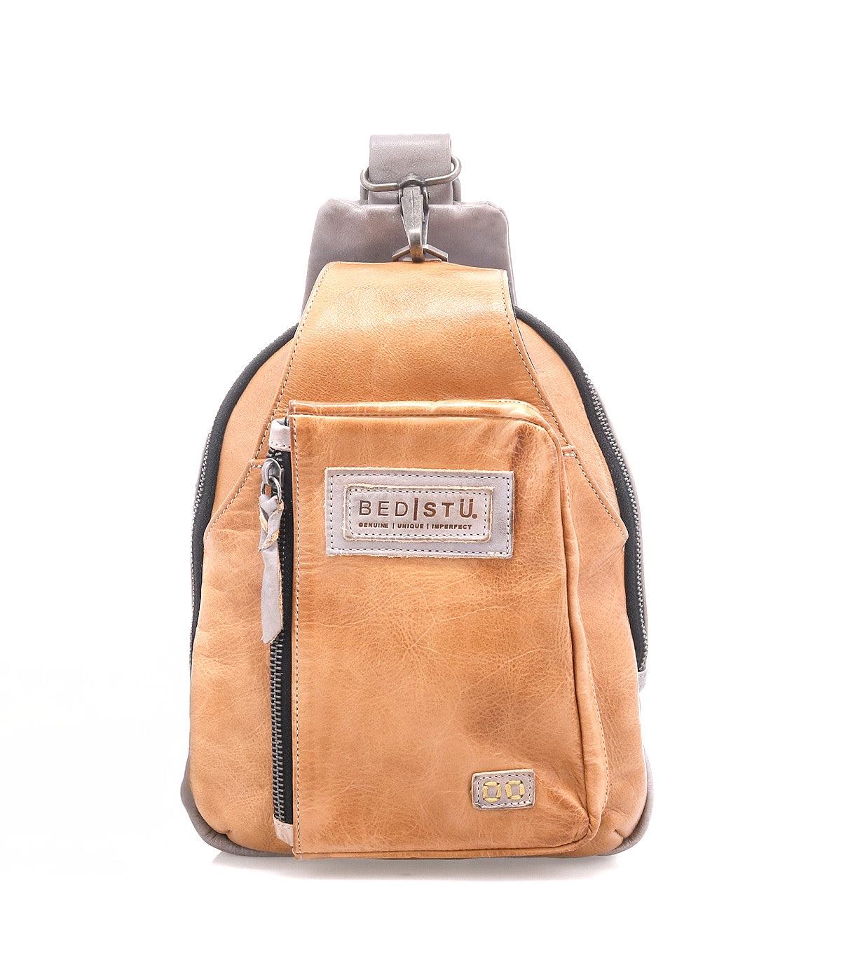 The Beau backpack by Bed|Stü is a compact tan leather sling with a front zipper pocket, signature "BED|STU" patch, and a single adjustable strap, shown against a white background.