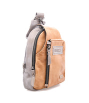 The Beau by Bed|Stü is a tan and gray leather sling backpack featuring a front zip pocket, top handle, and a visible Bed|Stü brand patch on the front, delivering the ideal combination of style and function in a compact design.