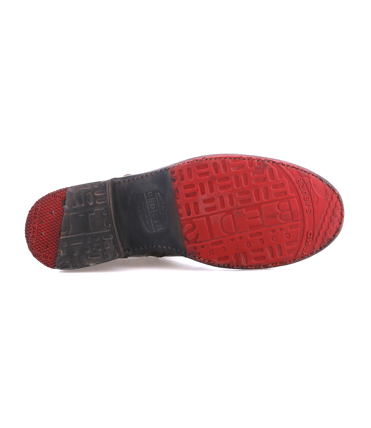 The image displays the bottom view of the Bed|Stü Becca dress shoe, showcasing its red rubber sole with textured patterns and a black heel—details inspired by the sturdy craftsmanship typical of an engineer boot.