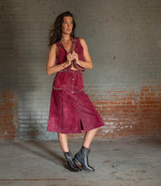 A woman stands indoors against a brick wall, wearing a sleeveless maroon dress with metal studs and Bed|Stü Bitsy black leather boots featuring a square toe and stacked heel.