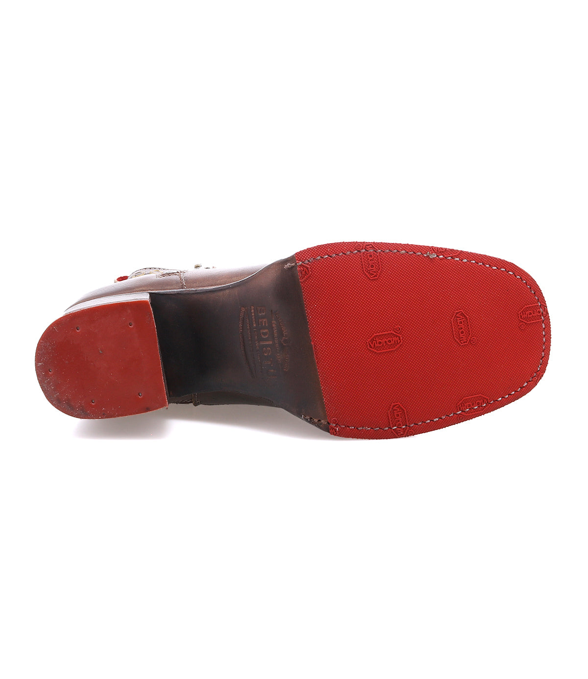 The image shows the bottom view of the Bed|Stü Bitsy brown leather dress shoe, featuring a red rubber sole and heel with brand markings and textured grip patterns—elements characteristic of quality leather boots. Its distinct stacked heel adds a modern touch that enhances the sophistication of the design.
