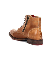 The Bed|Stü Bonnie II is a brown leather combat ankle boot featuring a cap toe, side zipper, decorative stitching on the heel, and a dark wood Goodyear-welted outsole, shown from a rear side angle.