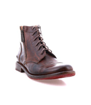The Bonnie II by Bed|Stü is a brown leather combat ankle boot with laces, a side zipper, cap toe, low heel, and an eye-catching red rubber sole, photographed on a white background.