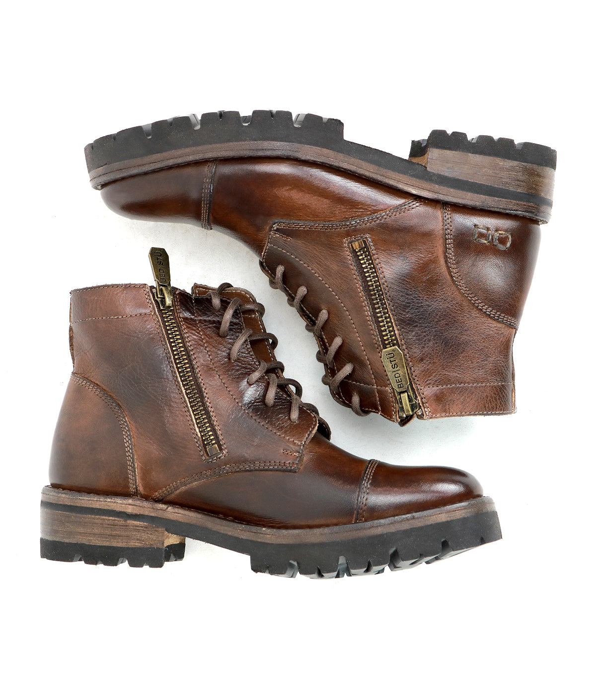 The Bed|Stü Bonnie IV is a pair of brown leather combat boots featuring dual side zippers, laces, and thick rubber soles for a secure fit, shown in a stacked side view.
