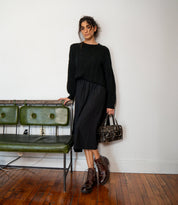 A woman wearing a black sweater, black skirt, and brown leather Bed|Stü Bonnie IV combat boots with dual side zippers, carrying a brown leather handbag.