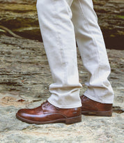 A person wearing light-colored pants and the timeless Bradley boots from Bed|Stü—crafted from brown leather with classic lace-up detailing—stands on a rocky outdoor surface, showcasing their versatility for everyday wear.