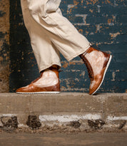 Wearing Bed|Stü's Breath statement sneakers, a person stands on a concrete step in tan pants, framed by a textured blue brick wall.