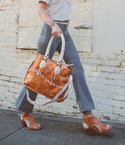 A person walks on a sidewalk wearing striped pants, a white t-shirt, heeled sandals, and carrying the Bruna two-toned leather bag with padded straps by Bed|Stü.